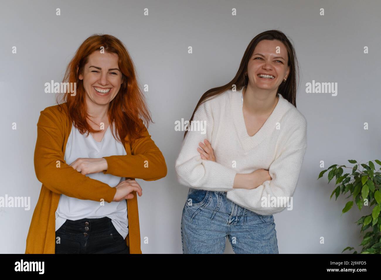 Glückliche zwei Frauen im Alter von 20s 40s über einer weißen Wand. Mitarbeiter in legerer Kleidung, die auf die Kamera schauen. Frau mit langen Haaren, fröhliche Freiberuflerin Stockfoto
