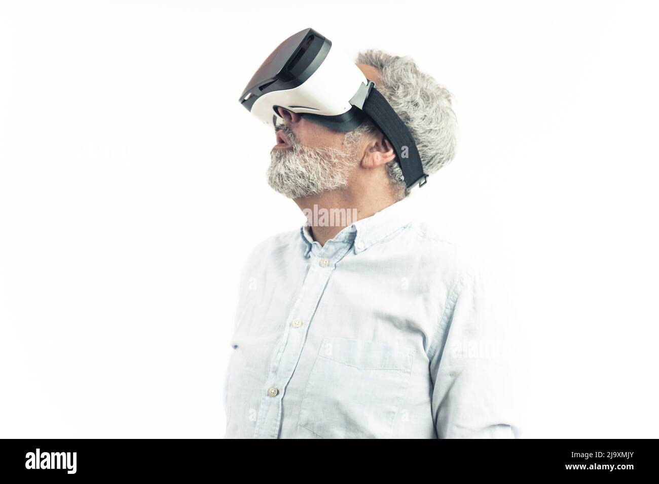 Virtual Reality für alle. Staunender europäischer silberhaariger Erwachsener in einem Hemd mit professioneller VR-Brille auf weißem Hintergrund. Einzelaufnahme. Hochwertige Fotos Stockfoto