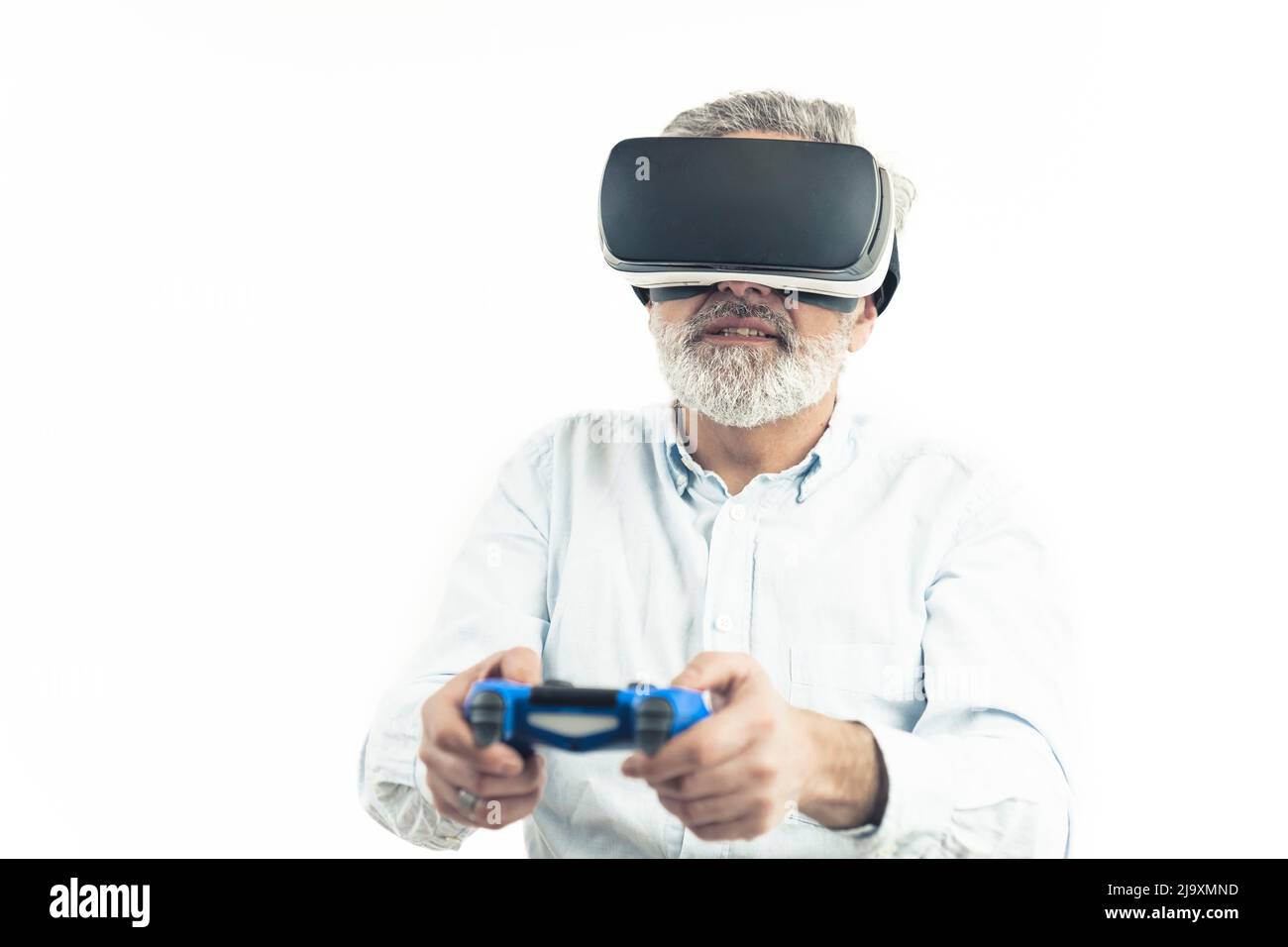 Kaukasischer Mann mittleren Alters mit silbergrauem Haar, das Virtual Reality Googles trägt und einen blauen Gamepad hält. Isoliert auf Weiß. Hochwertige Fotos Stockfoto