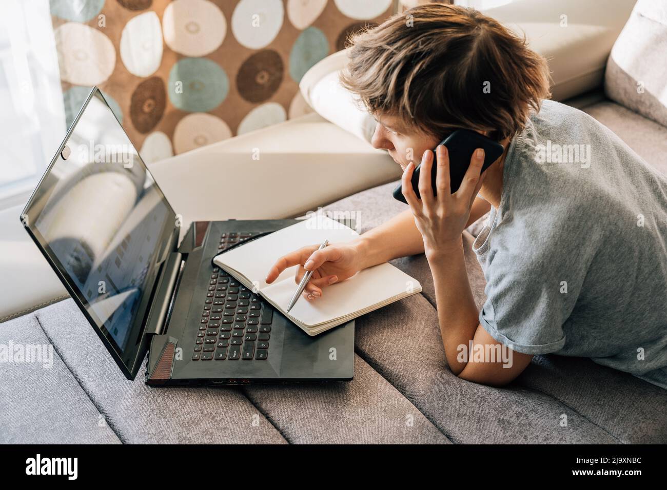 Frau spricht am Telefon und nimmt sich Notizen, während sie von zu Hause aus arbeitet Stockfoto