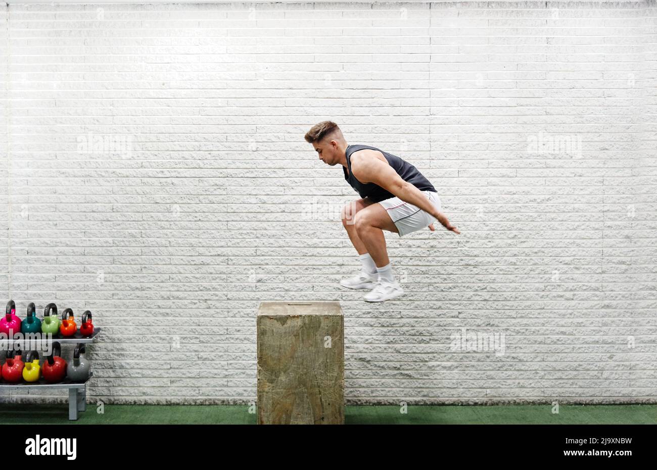Der junge Mann springt mitten in der Luft auf der Sportbox, die Arme reichen nach außen Stockfoto