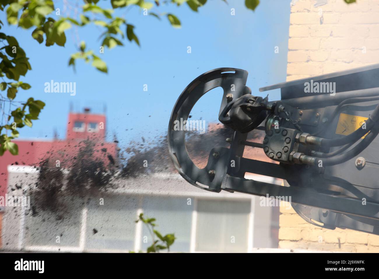 Das Straßenfräsfahrzeug lädt gefrästen Asphalt in einen Muldenkipper in einem engen Innenhof mit alten Häusern. Stockfoto