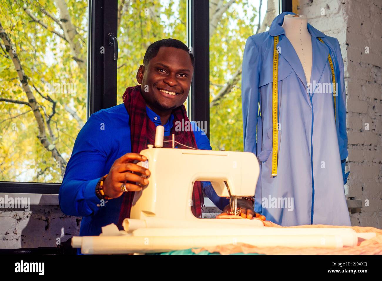 Porträt eines schönen afrikanischen Mann Näherin mit Nähmaschine.Afrio amerikanischer Mann stilvolle Designer arbeiten in Schneiderwerkstatt Schaufensterpuppe Mantel, Tisch Stockfoto Porträt eines schönen afrikanischen Mann Näherin mit Nähmaschine.Afrio amerikanischer Mann stilvolle Designer arbeiten in Schneiderwerkstatt Schaufensterpuppe Mantel, Tisch Stockfoto