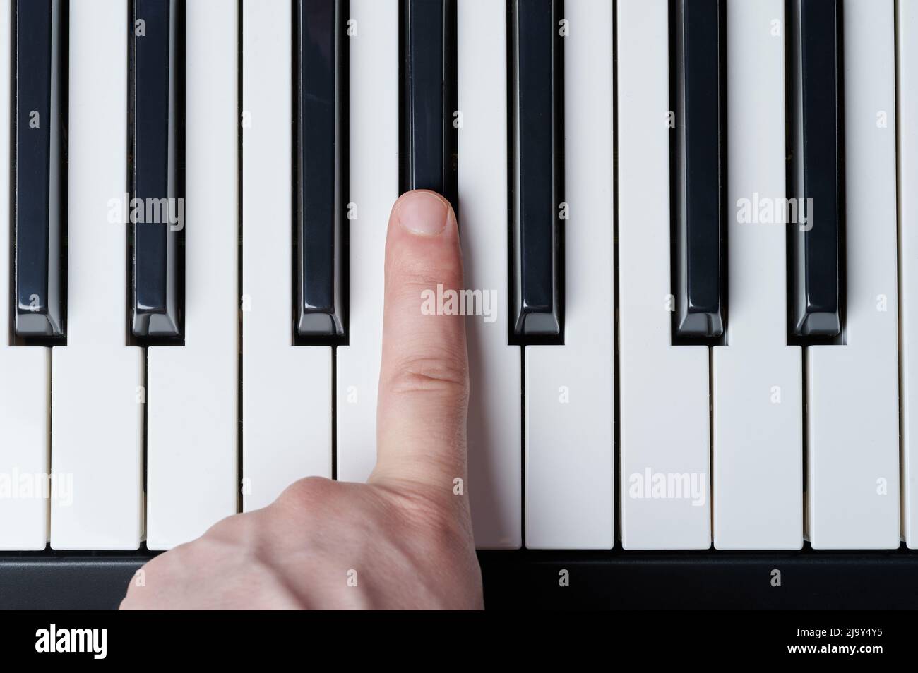 Drücken Sie mit dem Finger die schwarze Taste auf dem Klavier über der oberen Nahaufnahme Stockfoto