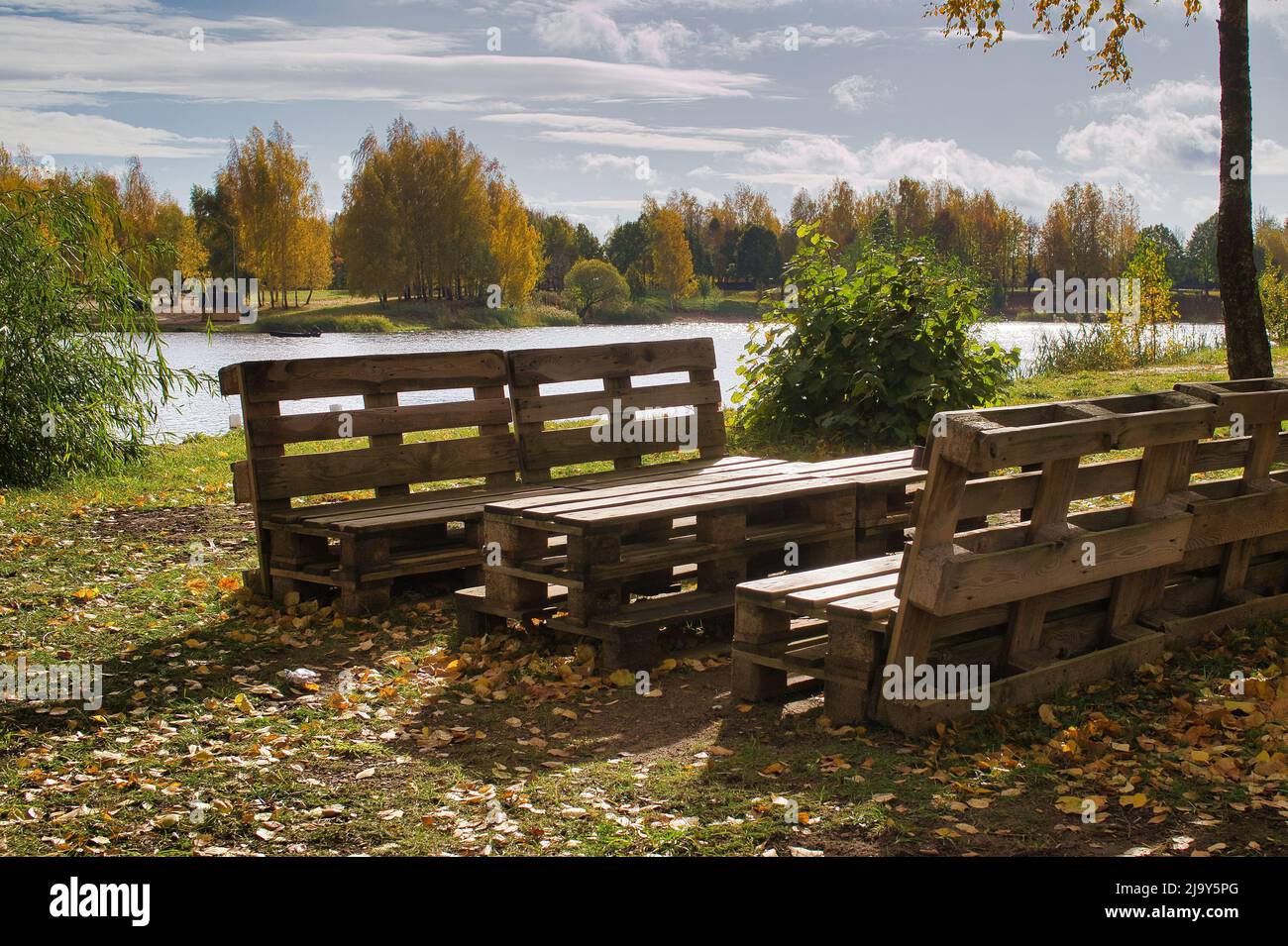 Gartenmöbel aus Holzpaletten am Ufer eines ruhigen Sees im Herbst Stockfoto