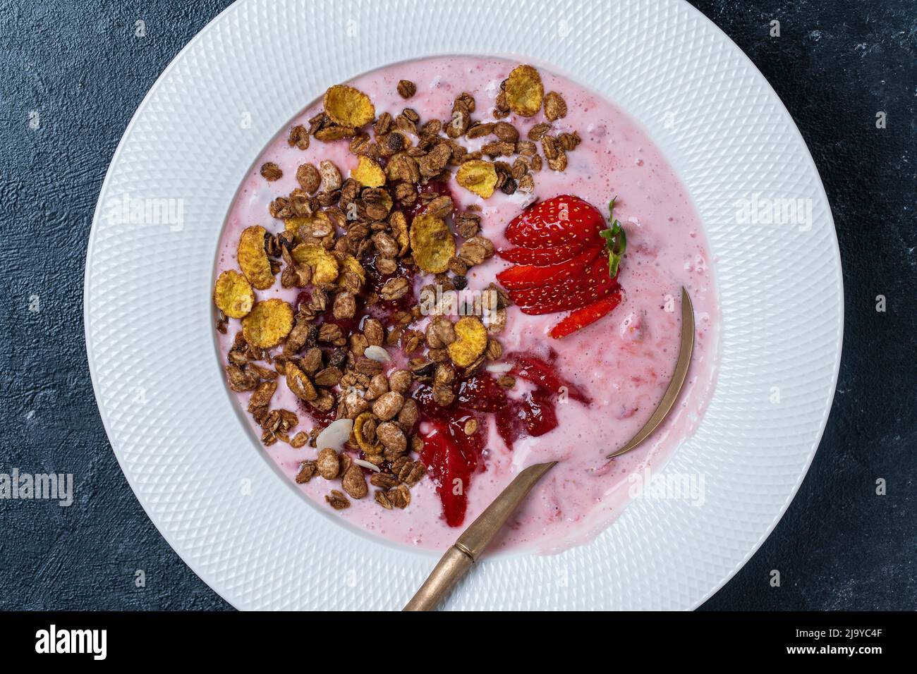 Weißer Teller mit roten Erdbeeren, Müsli und natürlichem Joghurt auf schwarzem Hintergrund, Nahaufnahme, Draufsicht Stockfoto