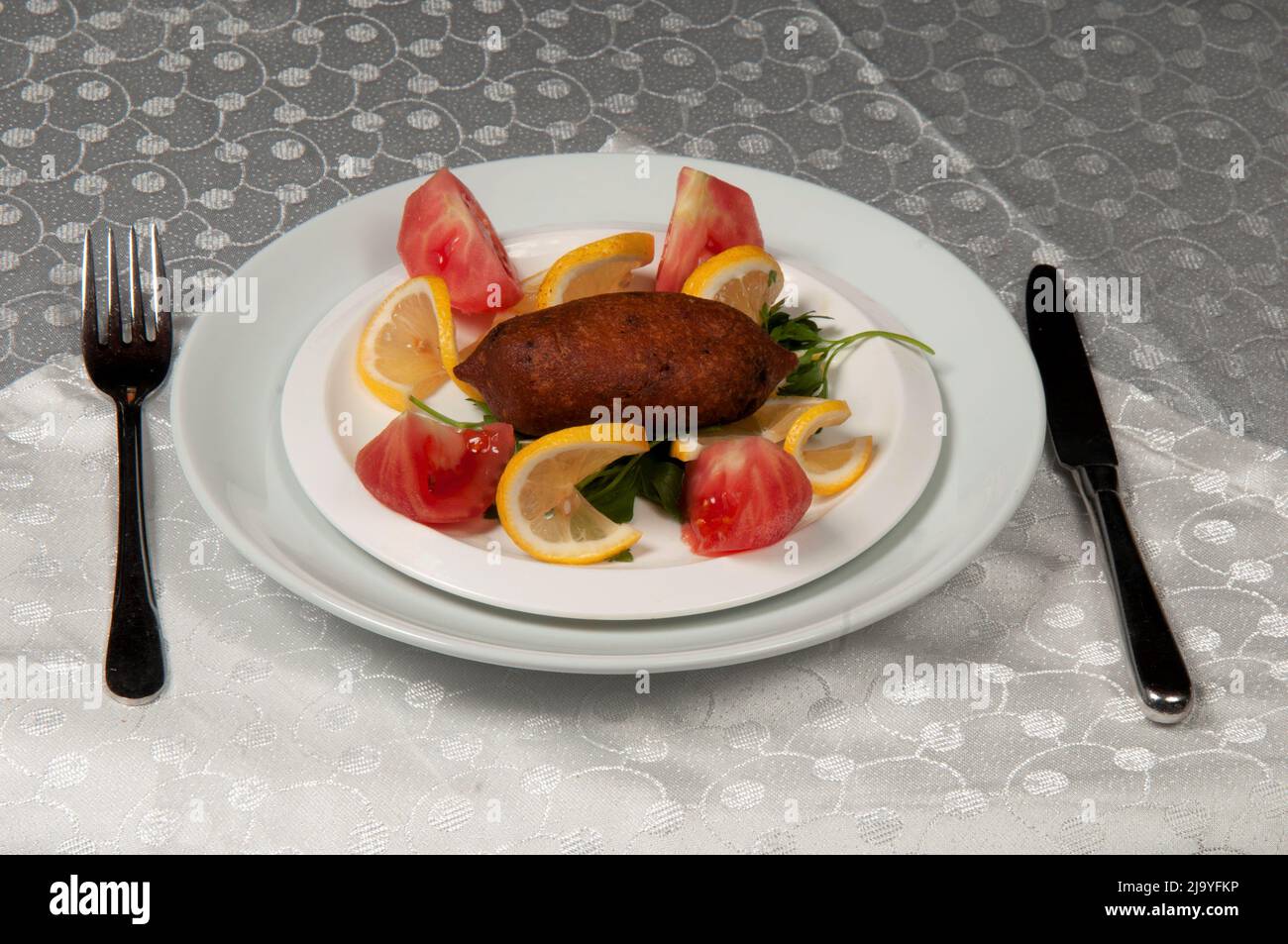 Ein Kibbeh, Zitrone und Tomate in einer weißen Keramikplatte. Das Gericht ist einzigartig in der Küche des Nahen Ostens. Stockfoto