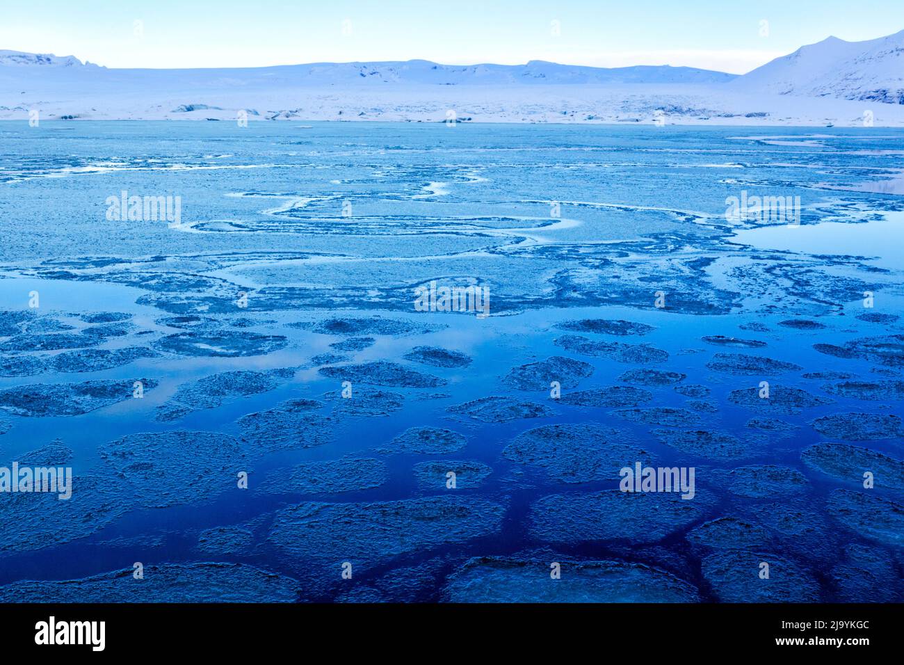 Ein Blick auf die Jökulsarlön-Eisberglagune im Winter mit einer „blauen Stunde“ am Morgen, ohne Eisberge. Die Lagune ist von einer zerbrochenen Schicht aus dünnem Eis bedeckt. Stockfoto