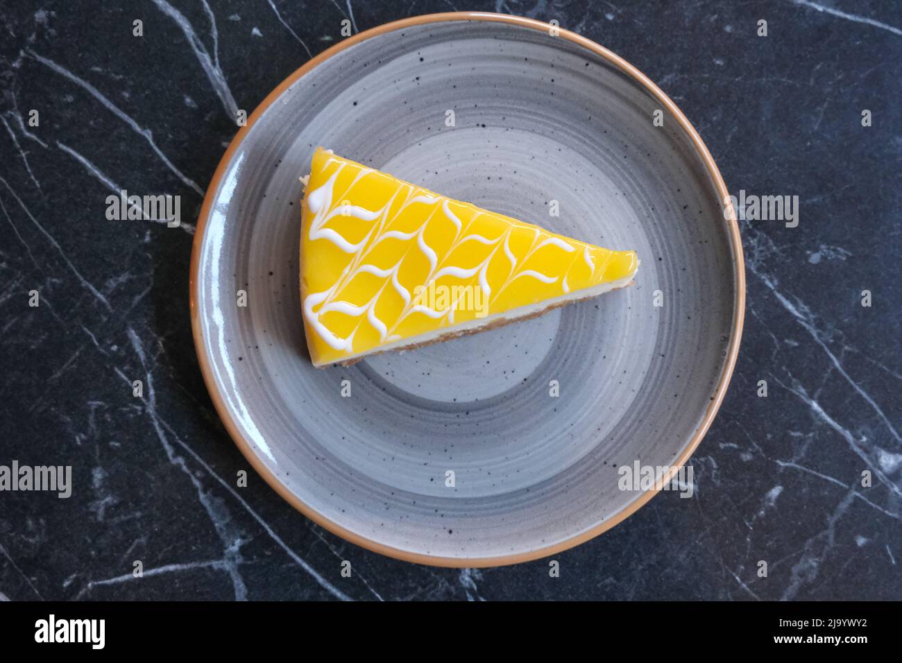 Eine Scheibe köstlicher Zitronenkäsekuchen auf dem Teller mit Marmorhintergrund. Ein Stück Käsekuchen von oben. Stockfoto