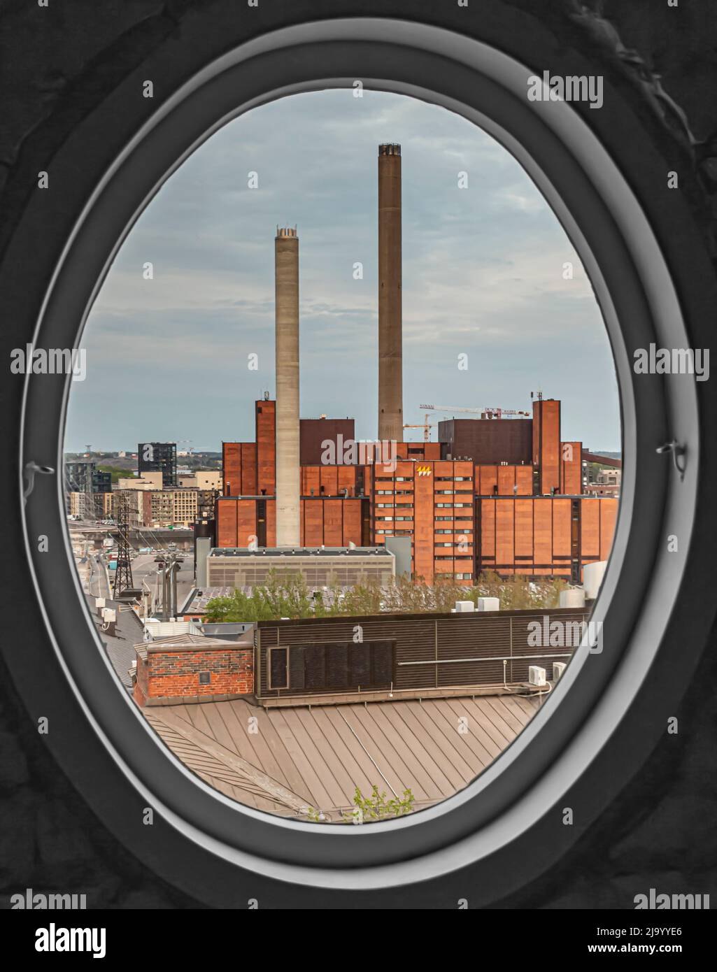 Das Kraftwerk Helen Ltd Hanasaari in Parrukatu, Sörnäinen, Helsinki, Finnland, wird durch ein ovales Fenster betrachtet. Stockfoto