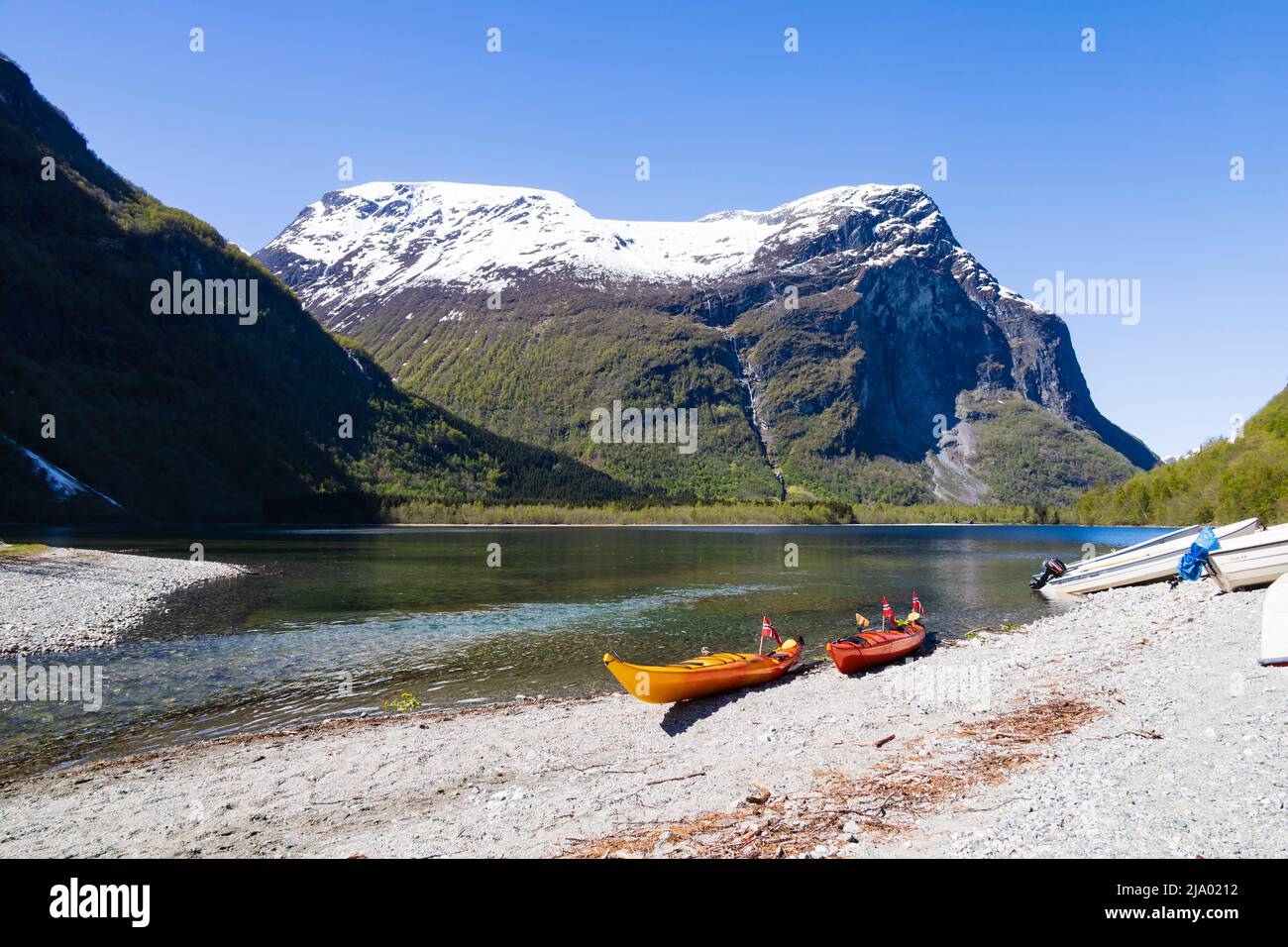 Zwei Kanukajaks am Ufer mit norwegischen Flaggen. See Lovatnet von Kjenndalstova, Norwegen. Schneebedeckte Berggipfel und klares blaues Wasser. Stockfoto