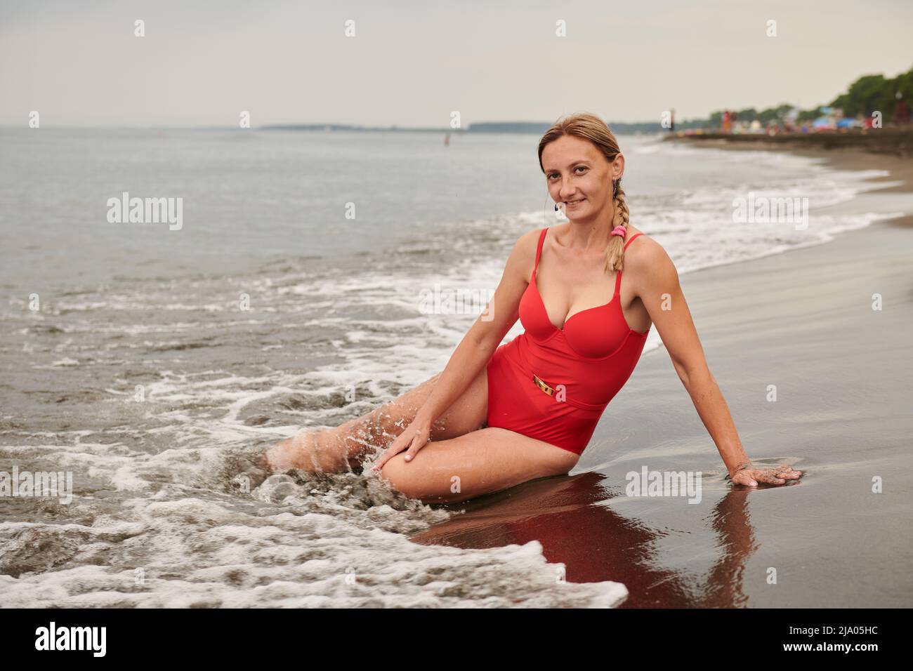 Brunette in einem roten Badeanzug liegt am Strand am Meer Stockfoto