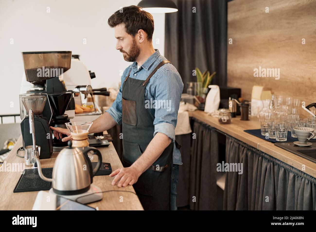 Der gutaussehende Barista mahlt Kaffeebohnen in der Kaffeemaschine Stockfoto