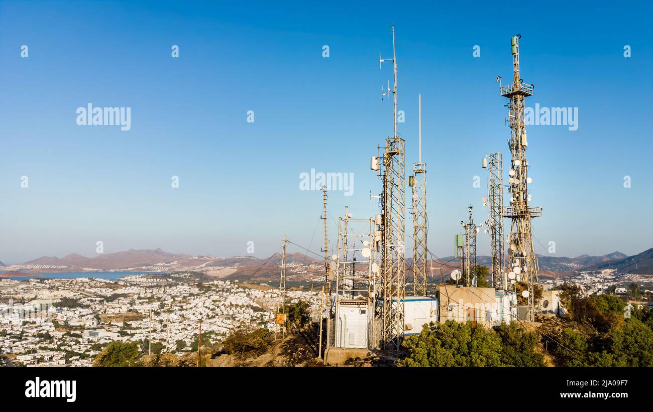 Blick auf Fernsehantennen des Telekommunikationsmastes bei Sonnenaufgang am Berg mit Stadt im Hintergrund. Netzwerkkommunikation Mit Antennenkelefon Stockfoto