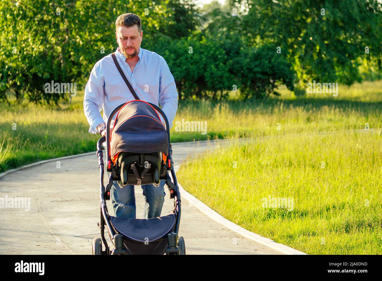 Ein gutaussehender Mann läuft mit einem Baby in einem Kinderwagen im Park Stockfoto