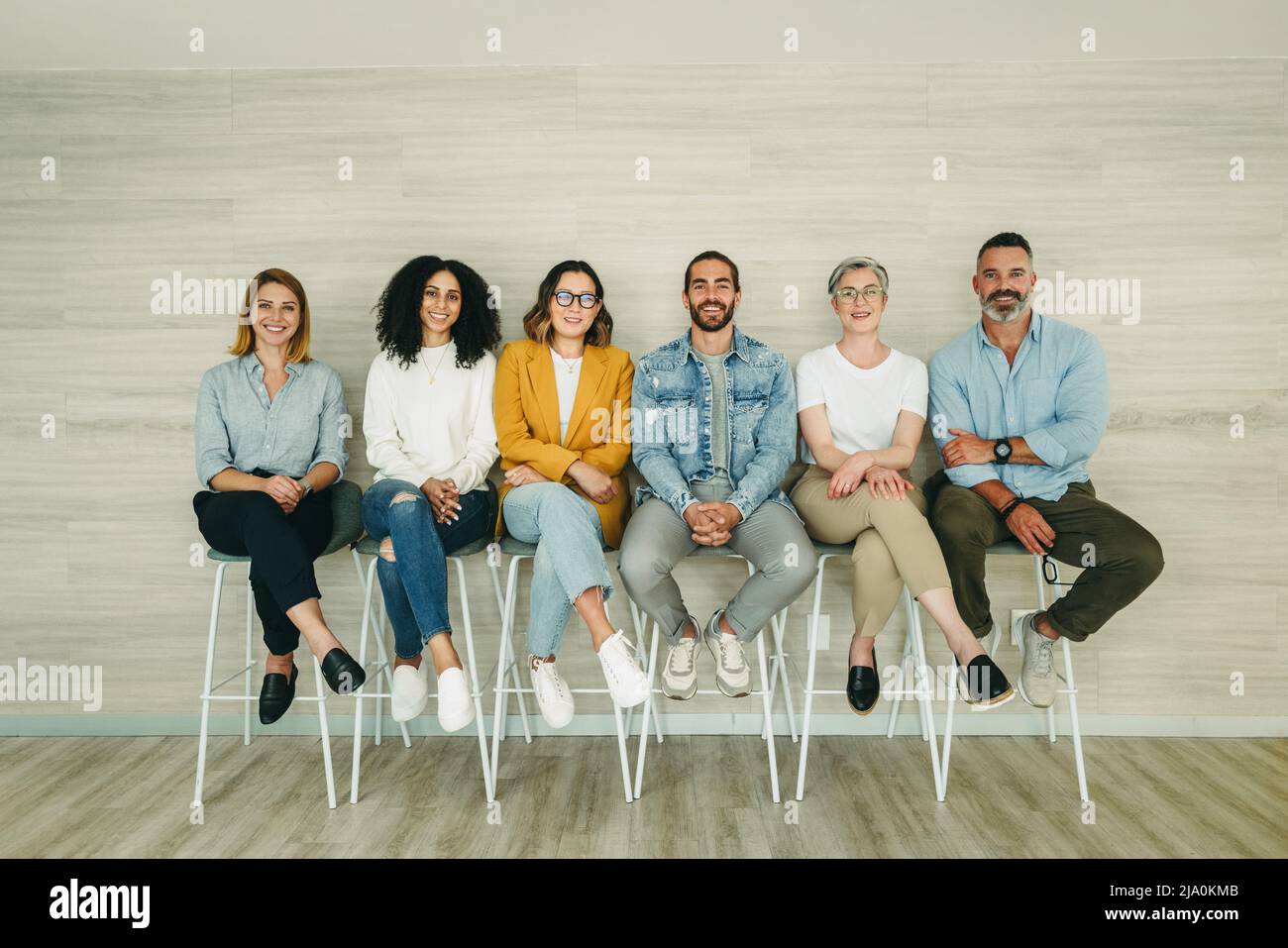 Fröhliche Bewerber lächeln an der Kamera, während sie in der Schlange für ein Interview sitzen. Gruppe multikultureller Geschäftsleute, die auf eine Gelegenheit warten Stockfoto