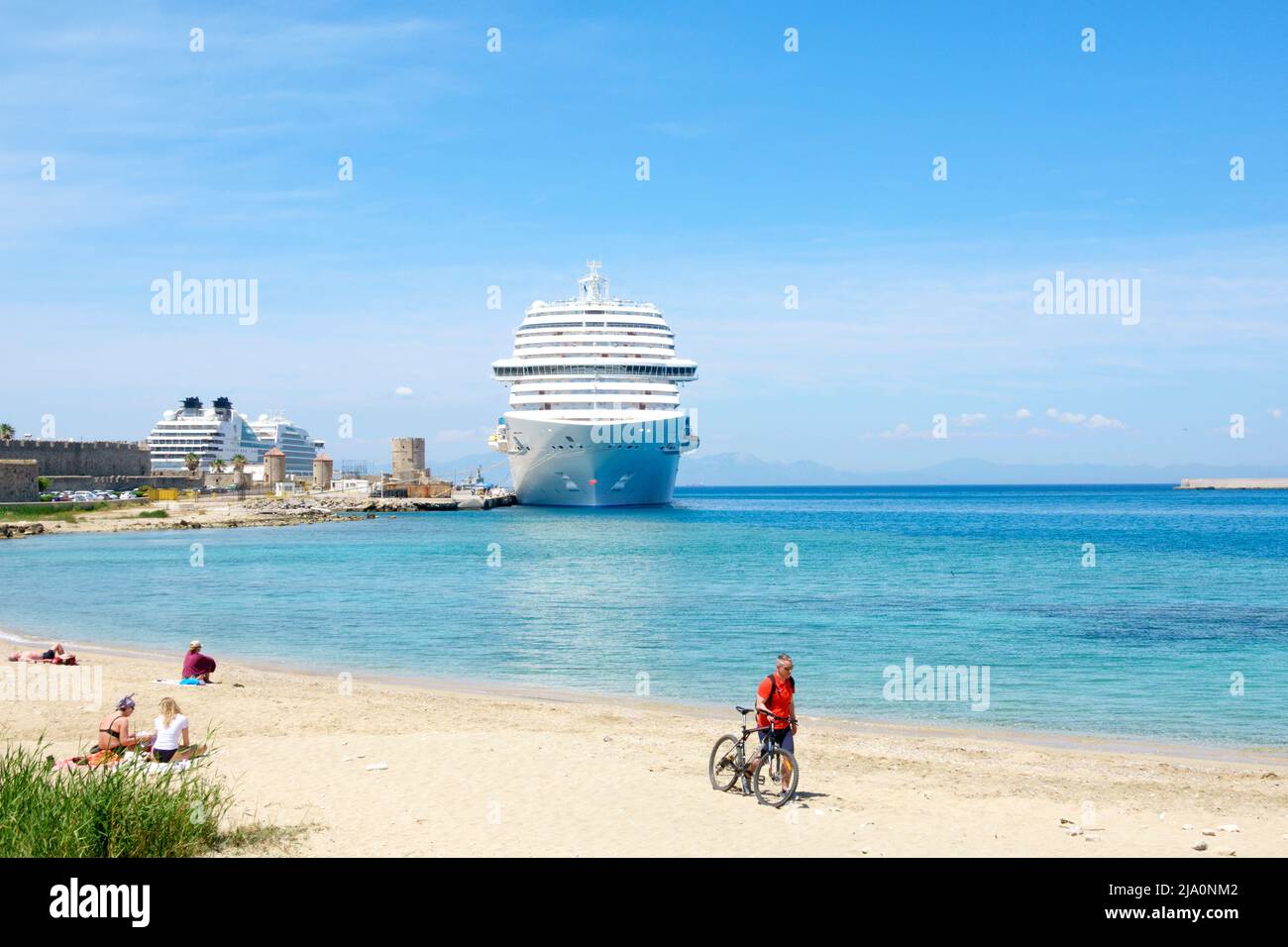 Blick über einen Strand auf das Costa Venezia-Schiff, das in der Mandraki Marina bei einem Besuch in Rhodos-Stadt, Rhodos, Griechenland, festgemacht wurde Stockfoto