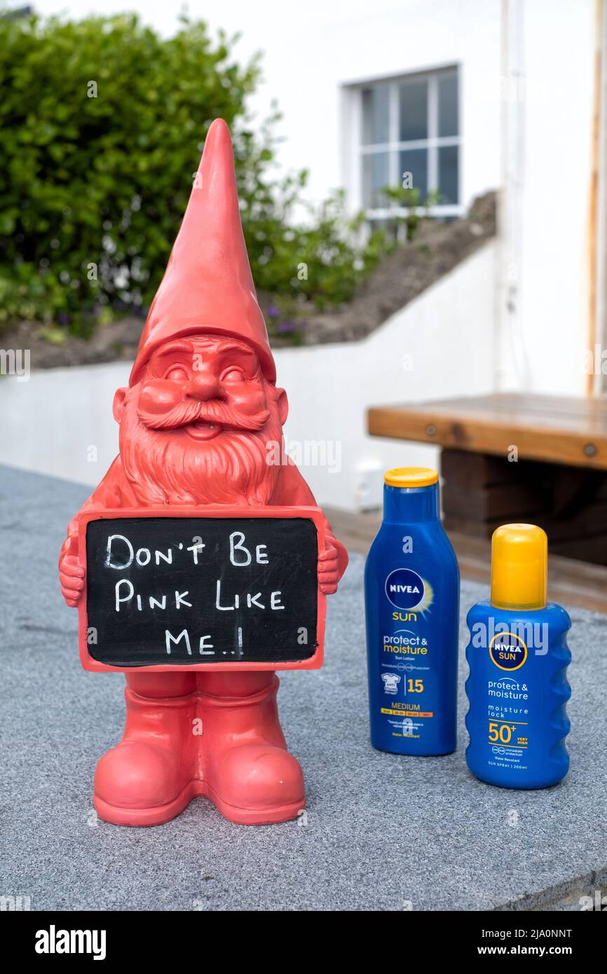 Ein komischer Garten-Gnome-Schmuck, der ein Schild für Sonnencreme vor einem Café zeigt. Der Besitzer hat Sonnenschutzmittel für Kunden zur Verfügung gestellt, die draußen sitzen können Stockfoto