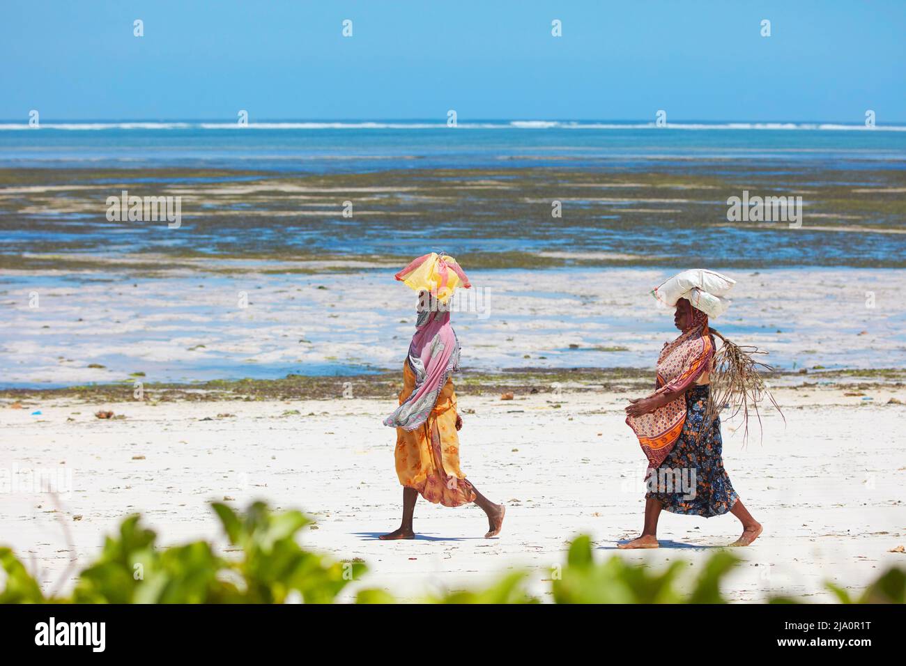 Frauen mit bunten Kleidern laufen am Strand von Jambiani, Sansibar, Tansania, Afrika. Stockfoto