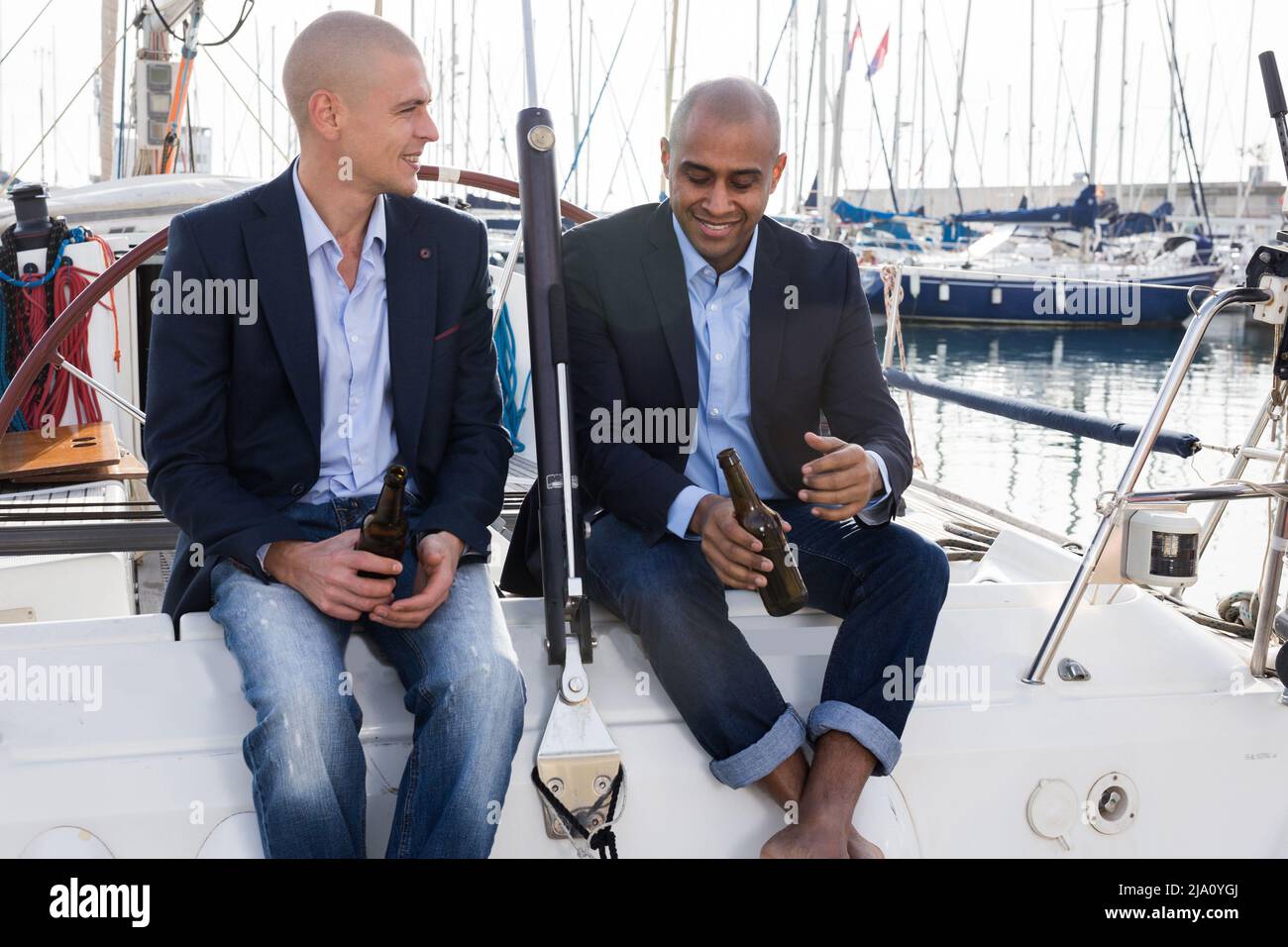 Lateinamerikanische und europäische Geschäftsleute sitzen und trinken Bier auf der Yacht im Seehafen Stockfoto