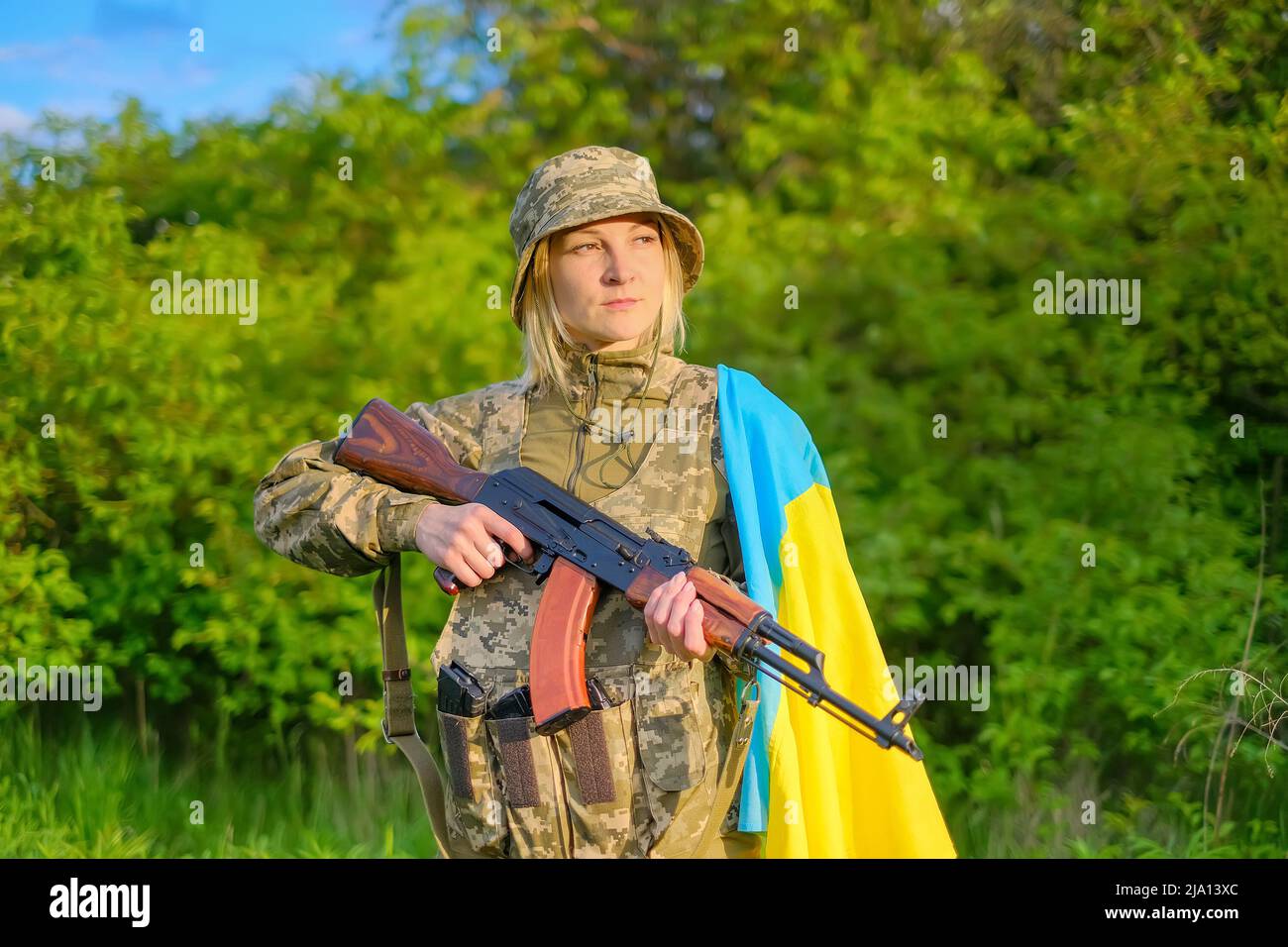 Porträt einer Soldatinnen mit Gewehr und ukrainischer Flagge auf der Schulter, die wegschaut Stockfoto