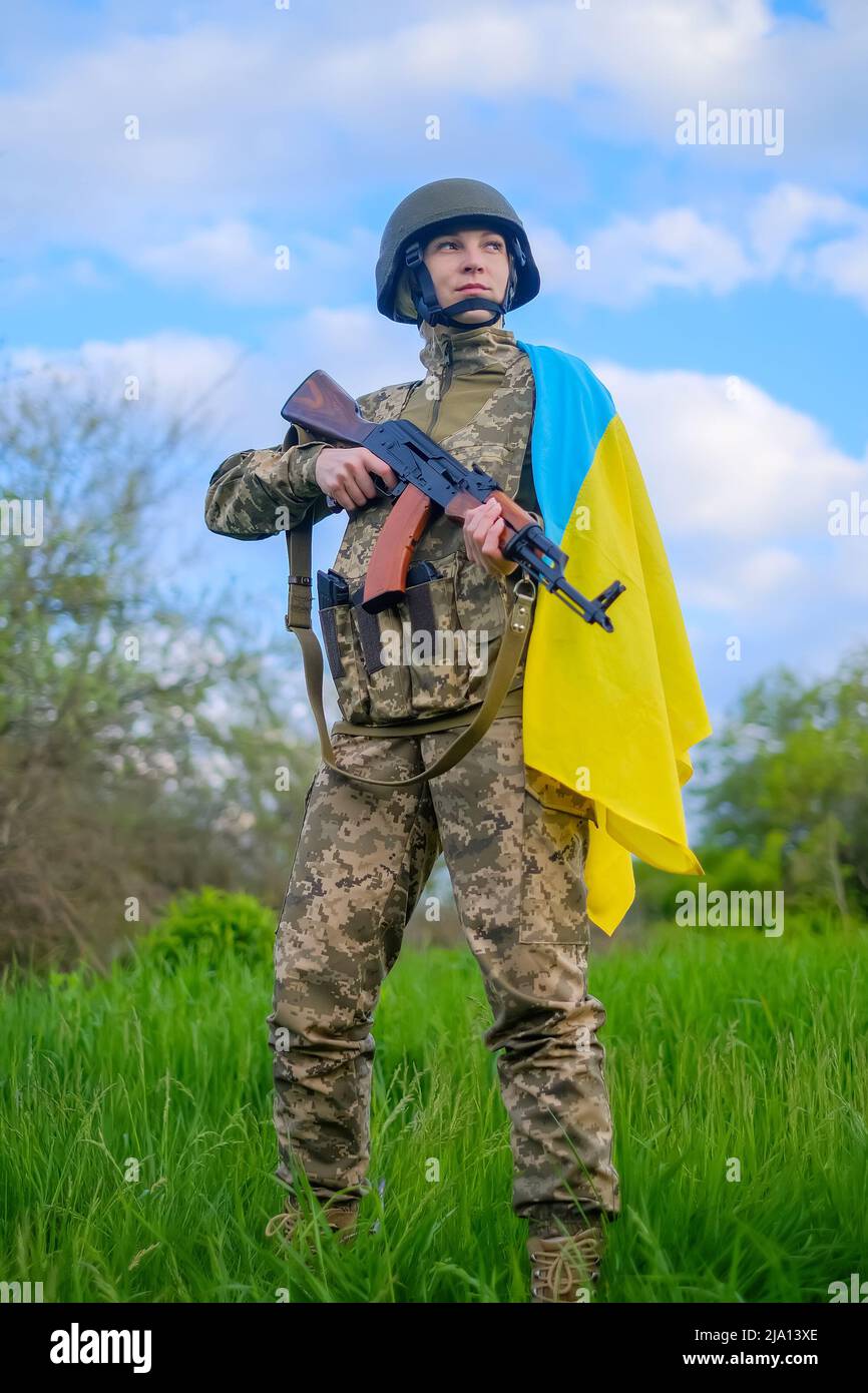 Lange Soldatin mit Waffe und ukrainischer Flagge auf der Schulter, die wegschaut Stockfoto