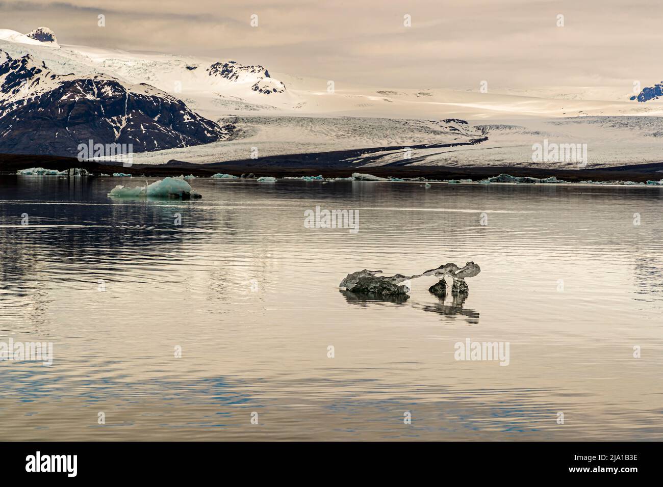Zwei Eisberge unterschiedlicher Größe treiben vor der Gletscherzunge des Breiðamerkurjökull in der Jökulsárlón-Lagune in Island unter einem Himmel, der von Wolken durchzogen ist. Mit etwa 284 Metern ist Jökulsárlón der tiefste See Islands, der sich seit 1934 durch den Rückzug des Gletschers gebildet hat. Stockfoto