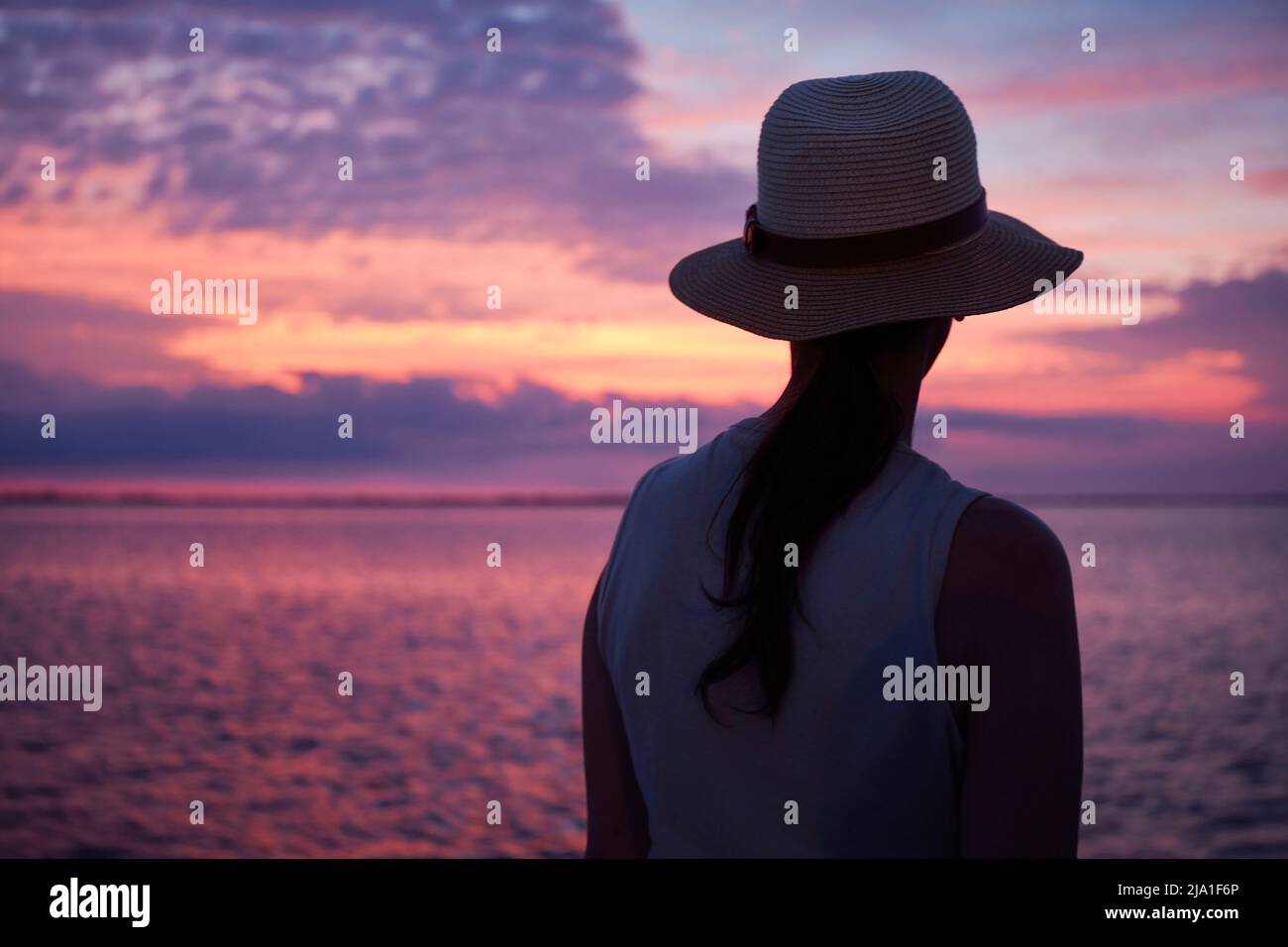 Ein Mädchen mit Hut, das die Dämmerung vom Hafen der Insel Martin Garcia, Rio de la Plata, Argentinien, aus beobachtet. Stockfoto