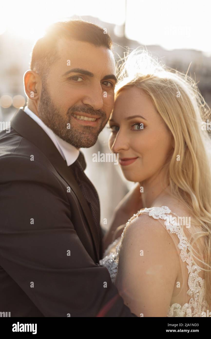 Vertikales Porträt Fröhliches und fröhliches romantisches Ehepaar, blonde Frau und schwarzhaariger Mann nach der Hochzeit, überkleidet Stockfoto