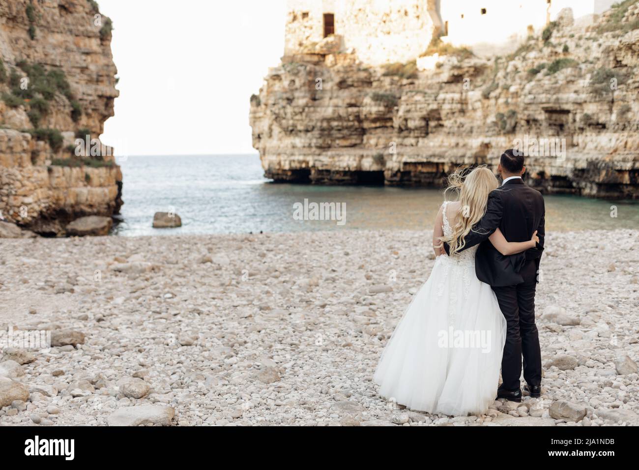 Rückansicht verheiratetes romantisches Paar in Hochzeitskleid und Anzug stehen am Strand, kontemplativ. Vacaion und Feiertagsveranstaltung Stockfoto