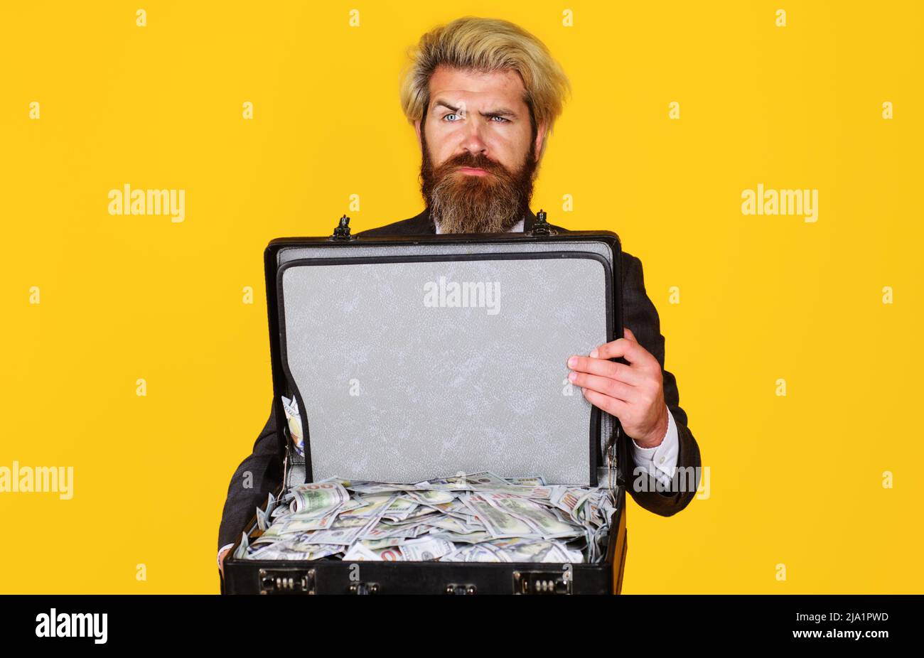 Millionär. Ernsthafter Mann mit Koffer voller Geld. Serious Geschäftsmann mit Aktentasche von Dollar. Stockfoto