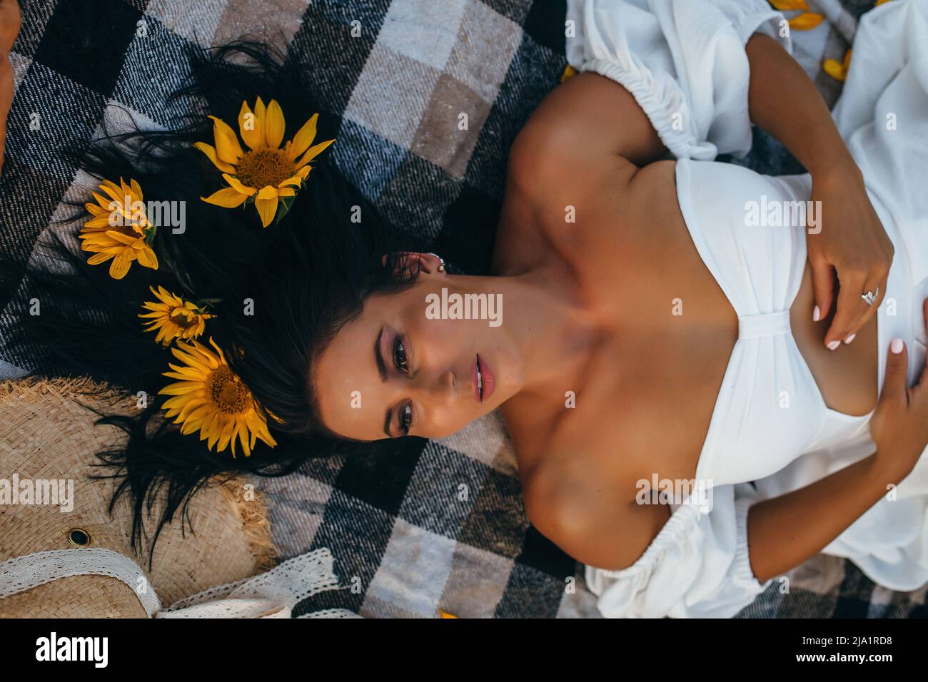 Schöne junge Frau in einem weißen Kleid in Sonnenblumen bei Sonnenuntergang Stockfoto