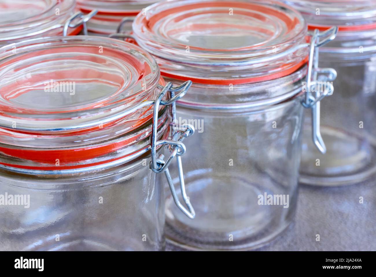 Nahaufnahme von leeren Gläsern oder Konservierbehältern mit orangefarbenem Verschlussring in einer Reihe. Konzept zur Erhaltung von Lebensmitteln. Stockfoto