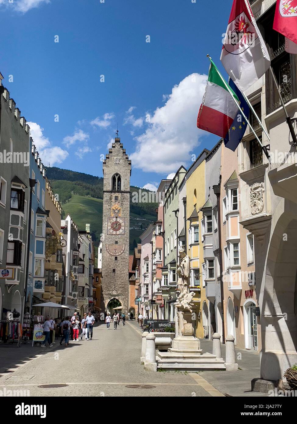 Zwölfter Turm, im Vordergrund der St.-Johannes-Nepomuk-Brunnen, darüber die italienische Nationalflagge, die Flagge Südtirols, die historische Neustadt Sterzing Stockfoto