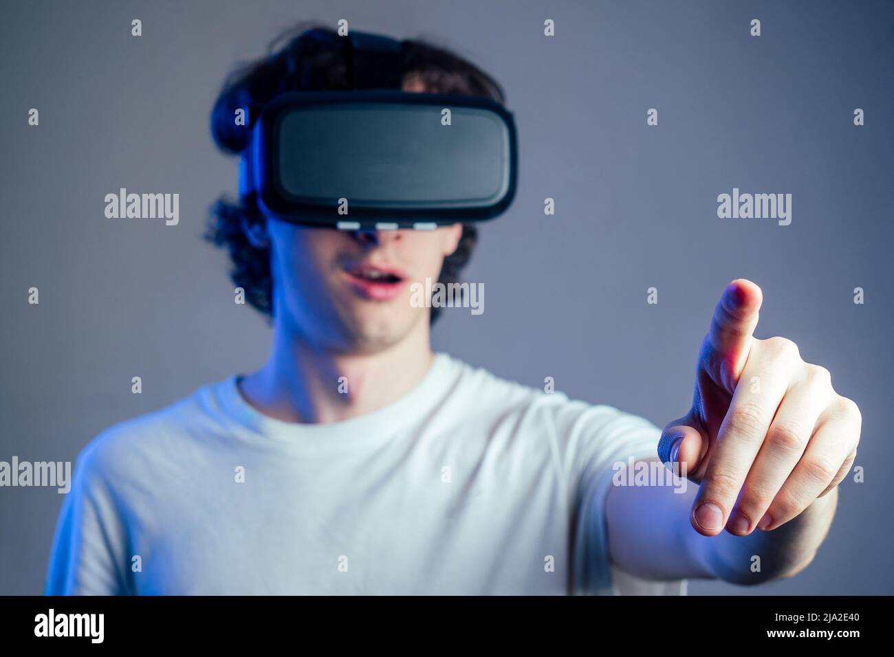Porträt eines jungen Mannes in der virtuellen Realität zeigt seine Finger grauen Wand Hintergrund. Das Konzept der Spiele in der Maske der virtuellen Realität Stockfoto