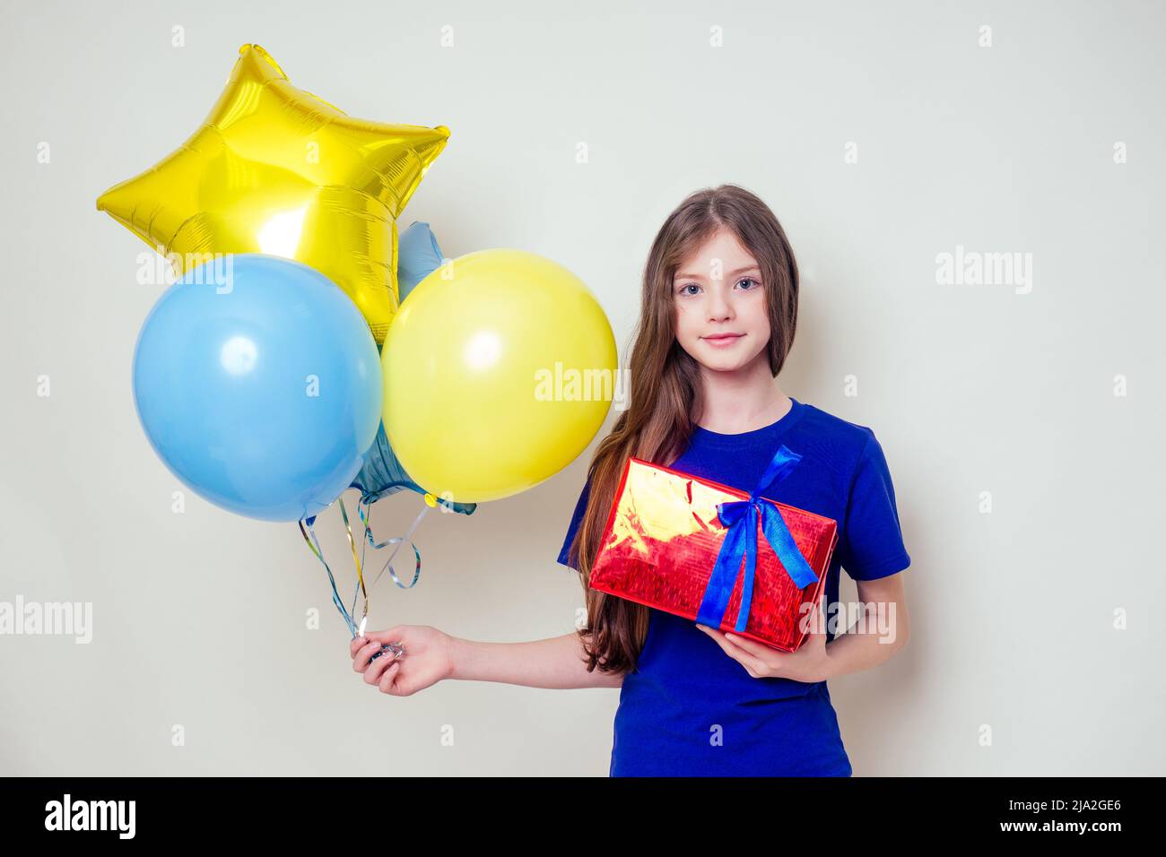 Nettes kleines Mädchen hält Helium blau, gelb und Gold Ballons und eine Box mit einem Geschenk Happy Birthday auf weißem Hintergrund im Studio .christmas und neu Stockfoto