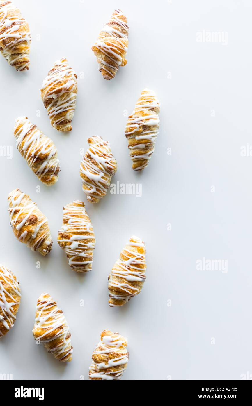 Mini-Zimt-Brötchen-Croissants, die vor einem hellen Hintergrund mit Glasur beträufelt sind. Stockfoto