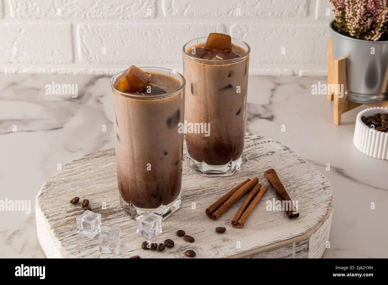 Zwei große Gläser mit Dalgon-Eiskaffee und Kaffeeeiswürfeln auf einem weißen Holzpodest und einem Marmortisch Stockfoto