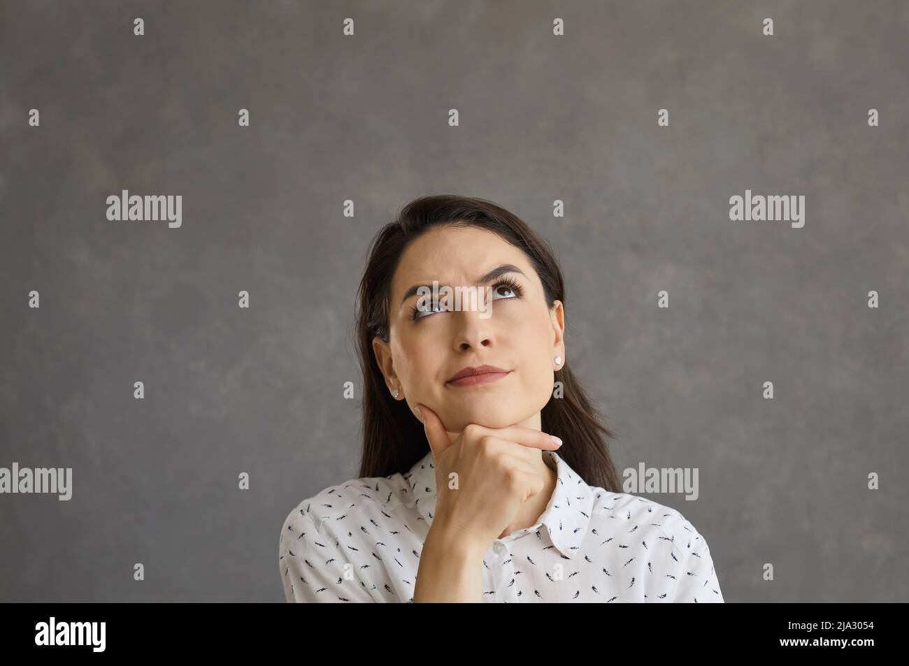 Verwirrte Frau voller Zweifel, die aufschaut und nachdenkt und versucht, eine Wahl zu treffen oder eine Frage zu beantworten Stockfoto