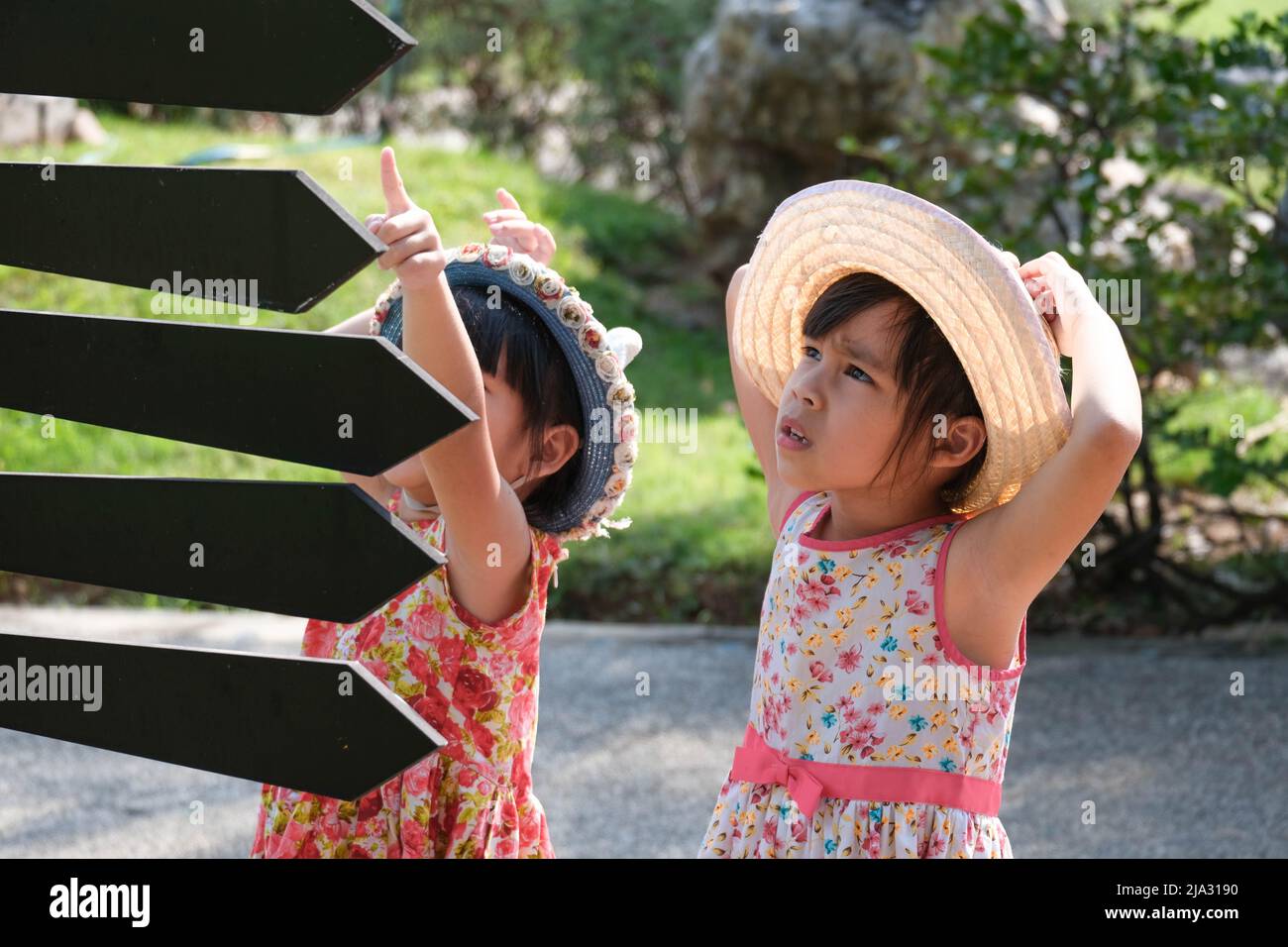 Kinder schauen auf Schilder mit Pfeilen, die auf verschiedene Orte im Park zeigen, um eine Wegbeschreibung zum Spielplatz zu finden. Stockfoto
