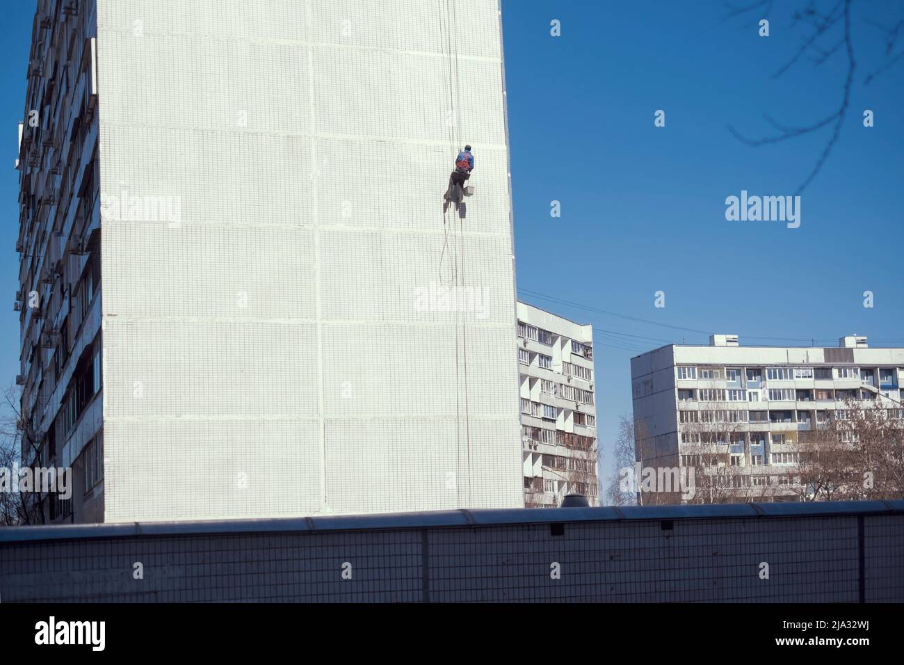 Industrieller Alpinist während der Gipsarbeiten auf der gefliesten Fassade des Gebäudes, Außenaufnahme Stockfoto