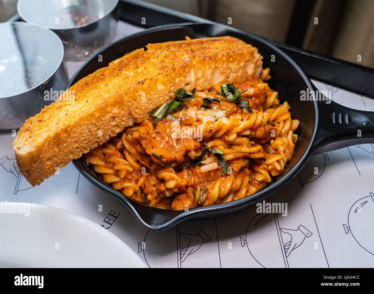 Fusilli Arrabiata Pasta und eine Scheibe Brot auf schwarzem Eisen Pfanne serviert. Stockfoto