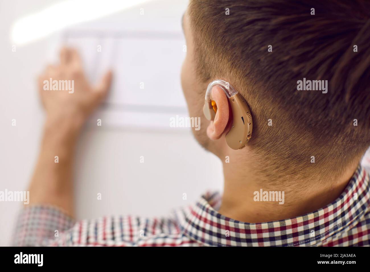 Nahaufnahme eines modernen Hörgerätemodells, das in das Ohr eines nicht erkennbaren jungen Mannes gesteckt wurde. Stockfoto