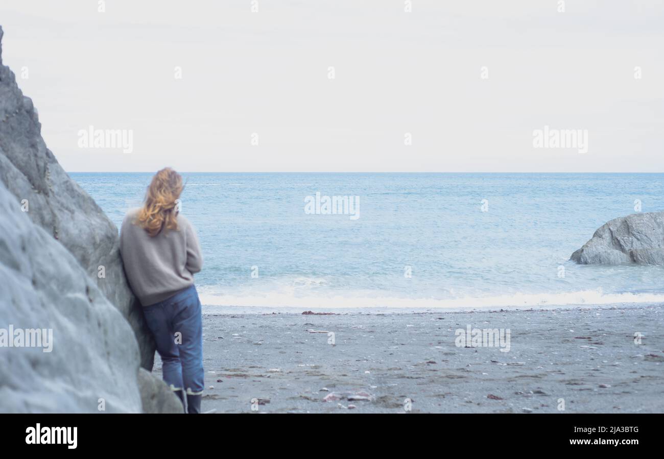 Junge Frau blickt auf das Meer an der Küste von Devon. Stockfoto