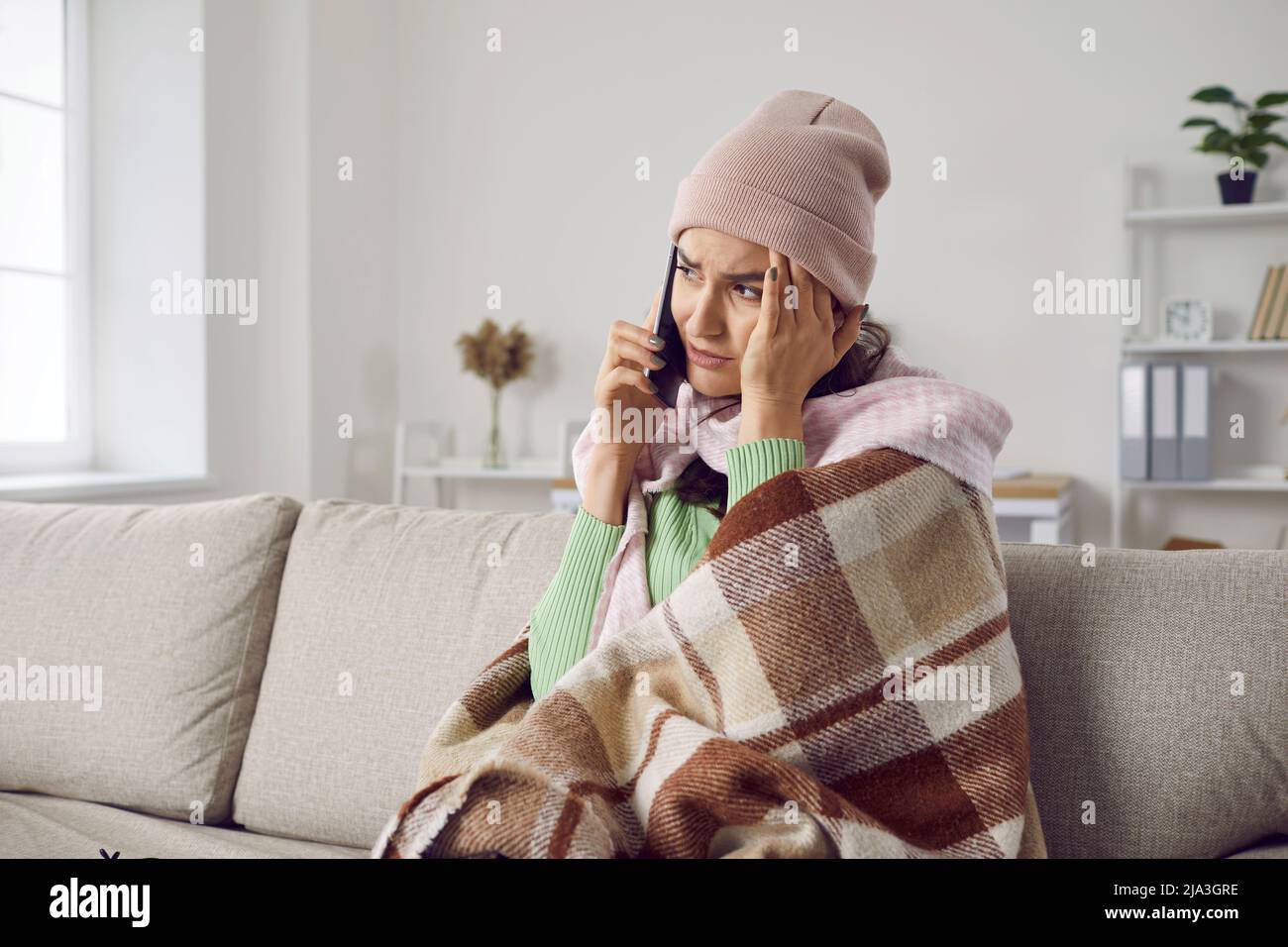 Unglückliche und erschöpfte Frau mit Erkältungssymptomen, die zu Hause sitzt, ruft ihren Arzt oder Krankenwagen an. Stockfoto