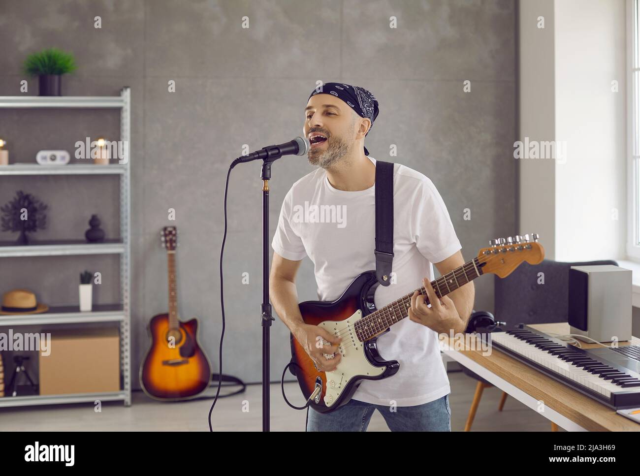 Begeisterter Sänger spielt E-Gitarre und singt im Heimstudio ins Mikrofon. Stockfoto