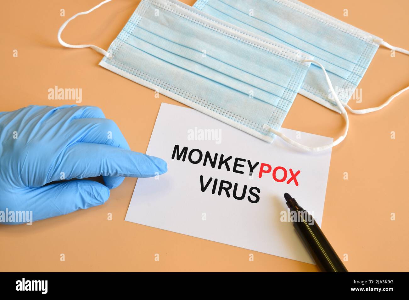 Doktor Hand in blauem Handschuh mit Stift zeigen monkeypox Virus Wörter auf weißem Papier mit Masken. Monkeypox auf weißem Papier. Medizinische und monkeypox Virus pan Stockfoto
