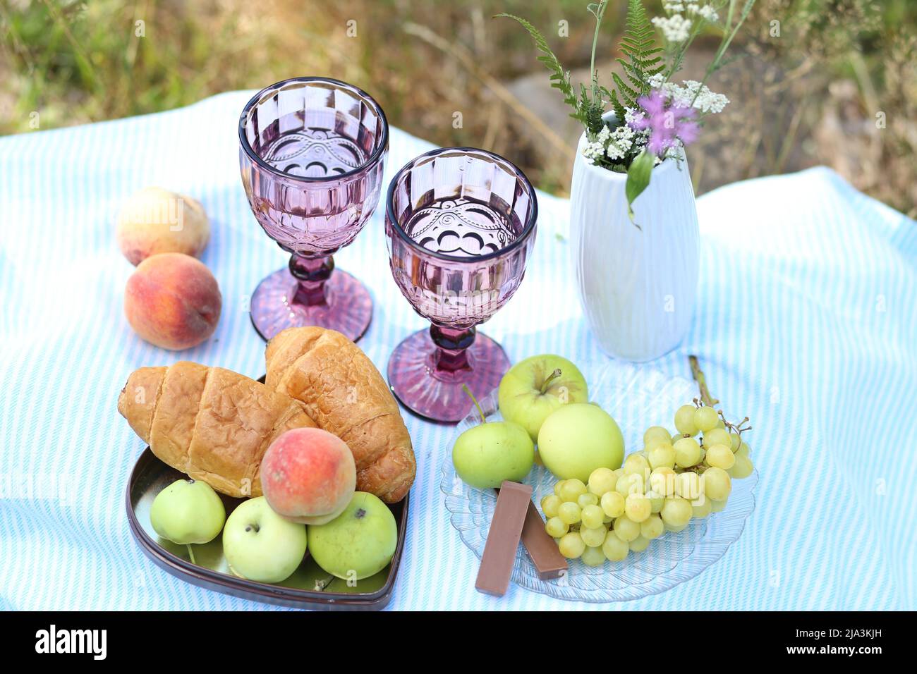 Romantisches Sommerpicknick: Croissants, Früchte, Schokolade, Trauben und Gläser Wein auf einer Decke. Hüttenkern-Ästhetik. Sommerstimmung Stockfoto