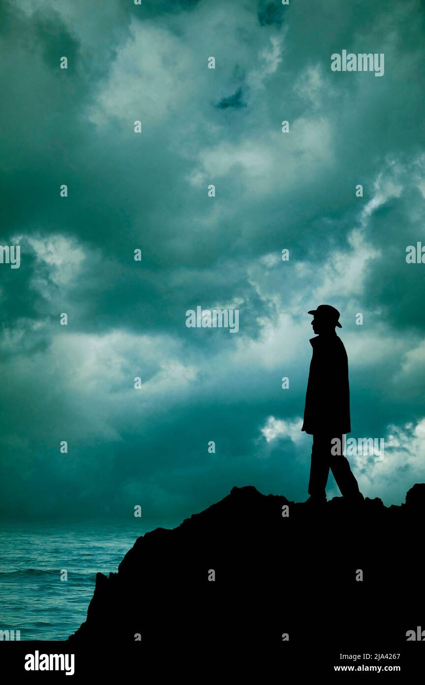 Silhouette eines Mannes mit Hut, der auf einem Felsen am Meer steht Stockfoto