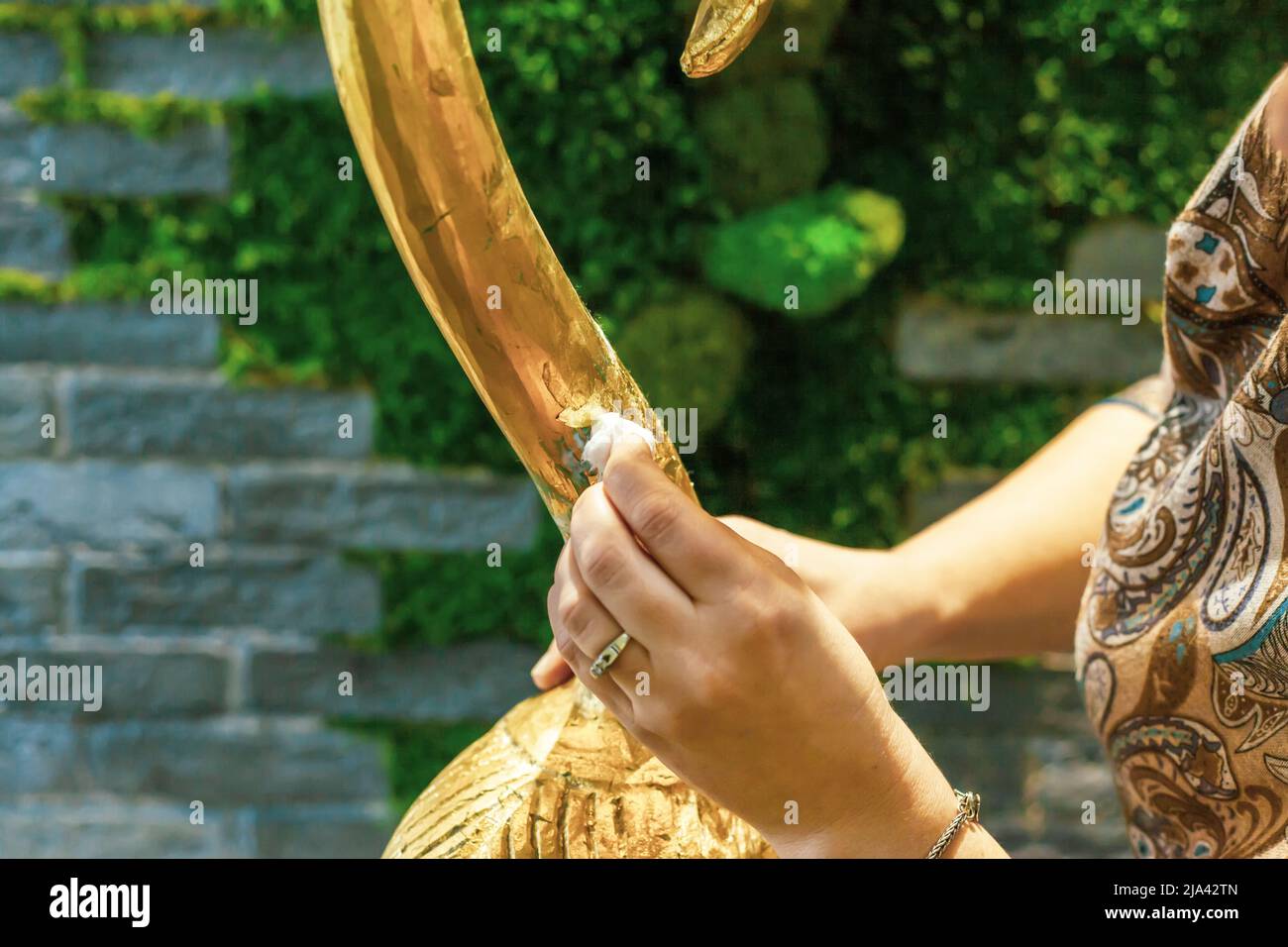 Eine Designerin restauriert und bedeckt eine hölzerne Flamingo-Statuette mit Goldfolie. Der Prozess der manuellen Vergoldung Stockfoto